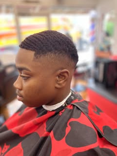 Finished cut in profile: short waves on top, a crisp line-up at the temple, and sides faded down to skin around the ear. The client wears a red cape with black spots and a white neck strip.